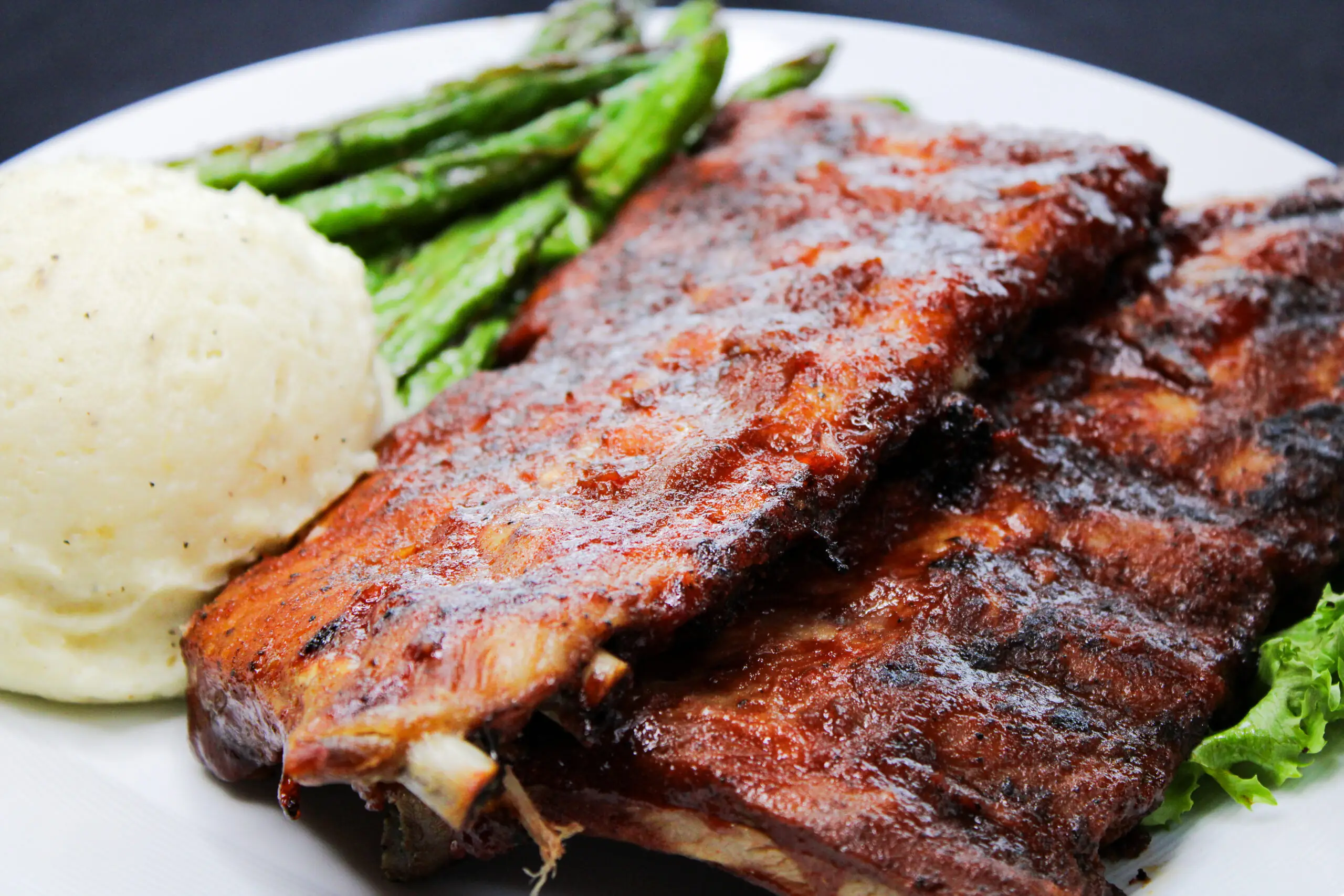 a plate of ribs, mashed potatoes and asparagus